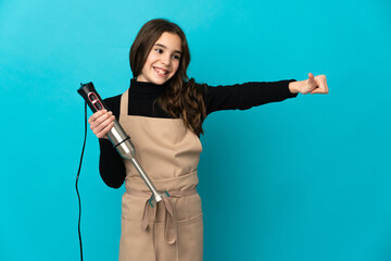 Little girl using hand blender isolated on blue background giving a thumbs up gesture