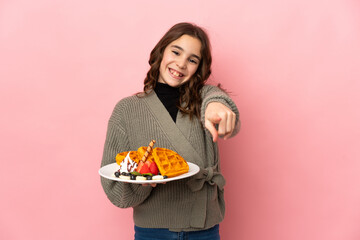 Little girl holding waffles isolated on pink background pointing front with happy expression