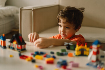 Cute boy is playing constructor at home. Kid playing block toys in home at nursery. Toddler having fun and building out of bright constructor bricks. Development and Construction Concept