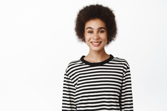 Portrait of beautiful young modern girl, black woman with afro hair, smiling and looking confident at camera, healthy people and lifestyle concept, white background