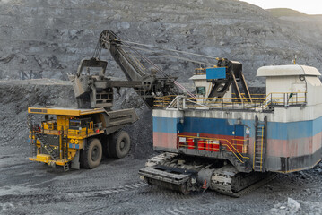 An electric excavator loads ore into a dump truck with a bucket. Night time. Gold mining site.