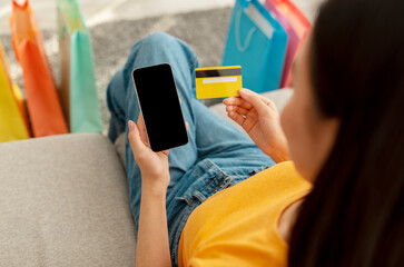 Online shopping concept. Millennial woman using smartphone with black screen and credit card, mockup