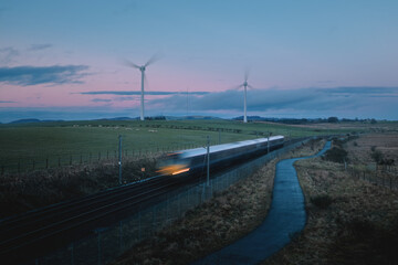 Moving blurred train across countryside and windmills in the field on the background in the...