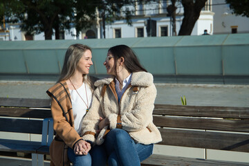 Real couple of young women, holding hands, sitting on a bench next to each other, looking into each other's eyes in an affectionate attitude. Concept lgtbiq+, lesbians, in love, inclusion.