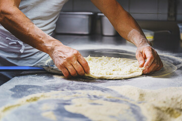 The Italian pizza maker prepares a margherita pizza by rolling out the dough with mozzarella on the...
