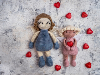 A pair of crocheted angels are held with pink hearts, a Valentine's Day card