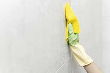 washing tiles on the wall. close-up of a female hand in a rubber glove and washing tiles on the...