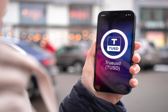 TrueUSD coin symbol. Trade with cryptocurrency, digital and virtual money, mobile banking. Hand with smartphone, screen with crypto icon close-up photo