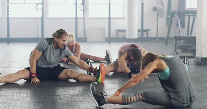 Stretching out those leg muscles. Fitness group of active young people doing a workout together at a gym. People at a health club doing a warmup exercise. Health, wellness and sport