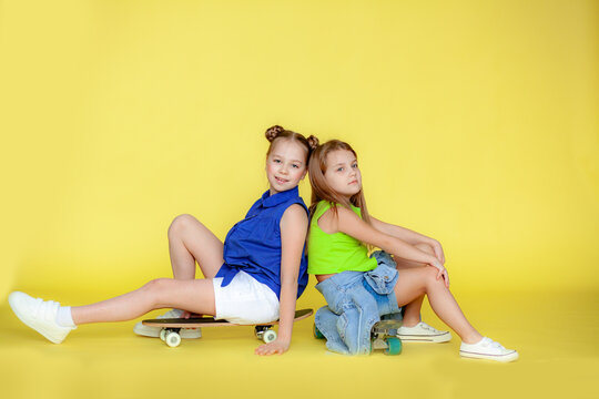 Funny little blonde girls 6-10 years old in everyday bright clothes pose isolated on the yellow background of the studio. The concept of a child's lifestyle. Layout of the copy space. Hold the skatebo