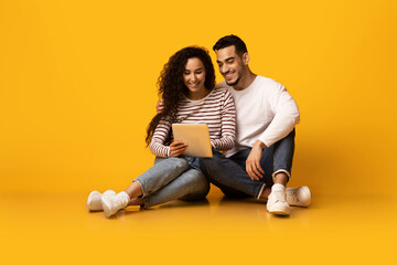 Cheerful Young Arab Couple Browsing Internet On Digital Tablet In Studio