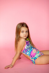 Obraz na płótnie Canvas A funny little blonde girl of 6 years old in a bright summer swimsuit poses alone on a pink studio background. The concept of a child's lifestyle. The location of the copy space. Background for your t