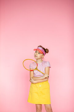 Photo of a girl with a happy positive smile, a sports tennis racket playing a game, isolated on a pink background