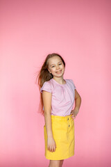 A funny little blonde girl of 10 years old in everyday bright clothes poses alone on a pink studio...