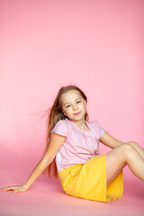 A funny little blonde girl of 10 years old in everyday bright clothes poses alone on a pink studio...