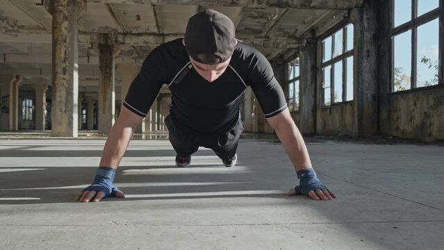 Boxer doing push-ups in abandoned building. MMA fighter training in elastic bandages. Sport concept in slow motion