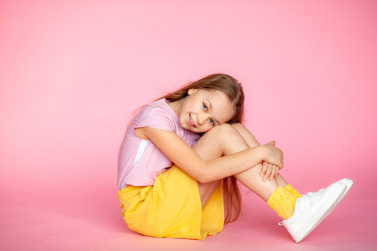 A funny little blonde girl of 10 years old in everyday bright clothes poses alone on a pink studio background. The concept of a child's lifestyle. The location of the copy space. Background for your t