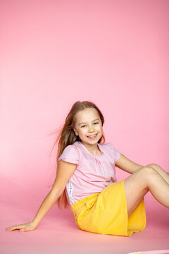 A funny little blonde girl of 10 years old in everyday bright clothes poses alone on a pink studio background. The concept of a child's lifestyle. The location of the copy space. Background for your t