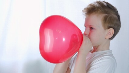 Valentine's Day, kids. Cute little boy on Valentine's Day or Mother's Day inflates a heart-shaped balloon on a white background.