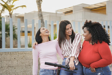 Young multiracial women having fun with electric scooter in the city