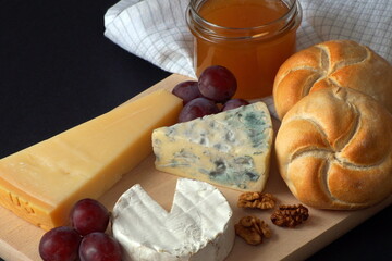 Cheese platter consisting of camembert cheese, blue cheese and parmesan with honey, grapes, nuts and freshly baked wheat buns