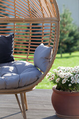 Patio arrangement with rattan cocoon armchair and flowers in ceramic pot.