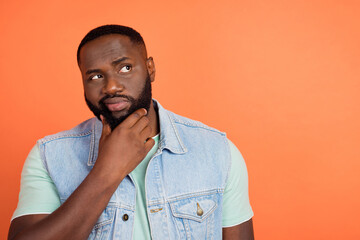 Photo of suspicious african guy dressed jeans waistcoat arm chin empty space isolated orange color...