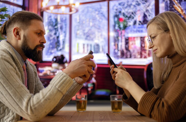 Side view of mature caucasian couple sitting at cozy cafe and looking at their smartphones. Modern lifestyles, internet addiction and loneliness concept.