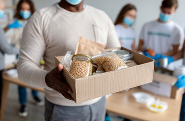 Senior black man holding box with donations food, cans and packages with grains and pasta, cropped