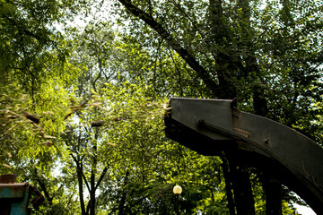 The work of a mobile shredder of dry branches and trees in a city park. Wood shredder. Workers recycle broken trees