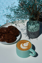 Morning cappuccino in coffee shop on summer terrace with flowers and chocolate cookies.