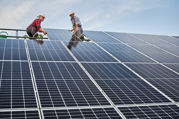 Low angle of two men solar technicians building photovoltaic solar panels under blue sky. Male...