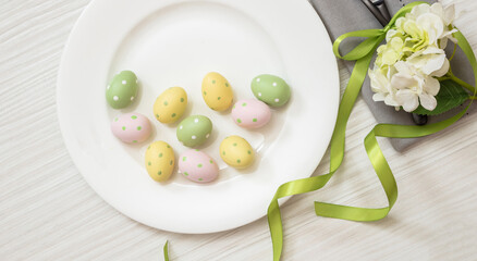 Easter table setting, Egg and flower decoration, plate and grey napkin on white wood, overhead
