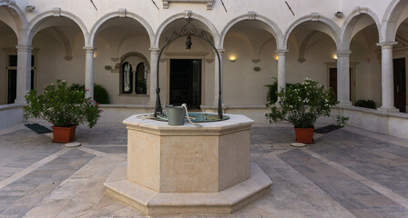 Old fountain on white mediterranean stone in monastery, surrounded with arches