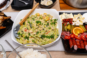 Green tagliatelle in gorgonzola sauce lying on a white plate with a wooden spoon on a table filled with food.
