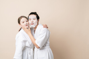 Fototapeta premium Happy Asian couple in bathrobe or spa suit doing sheet mask on face for facial treatment together on brown isolated studio background.
