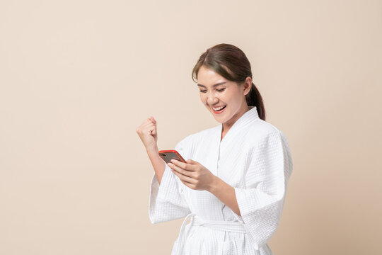 Portrait Beautiful young Asian women happy smile in bathrobe or spa suit and using smartphone trading or chatting on brown isolated studio background.