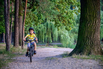 Portrait of happy toddler child boy riding on bike with helmet. He rides from a small hill, through a sandy forest path. Sport concept: kids ride bicycle first bike active toddler kid