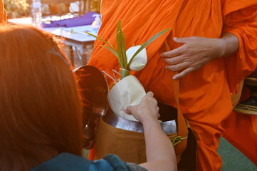 Hand holding a food in brown paper bag  bouquet of white lotus flowers and put into the monk's alms...