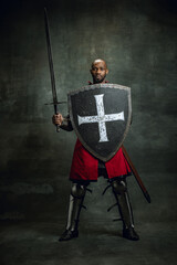 Portrait of medieval warrior, dark skinned bald knight with dirty wounded face holding shield and...