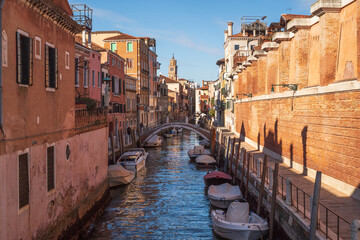 Fototapeta na wymiar Not ceremonial Venice, narrow canal with boats, bridge, textured houses, bell tower, morning light, unique atmosphere