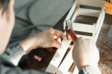Young Caucasian carpenter in working clothes makes wooden boxes in carpentry workshop. Hands with hammer close-up. Real scene. Workflow. Small business. Environmentally friendly packaging and
