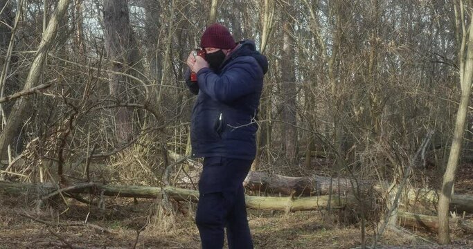 a photographer in a protective mask takes pictures on a vintage film camera against the background of a fallen pine tree, side view
