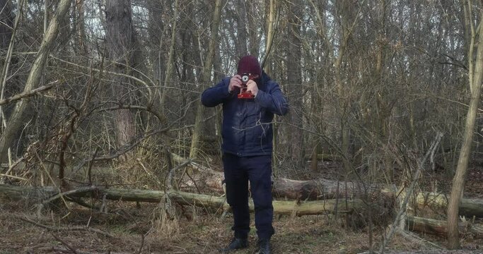 a man in a protective mask in a pine forest takes pictures on a retro film camera