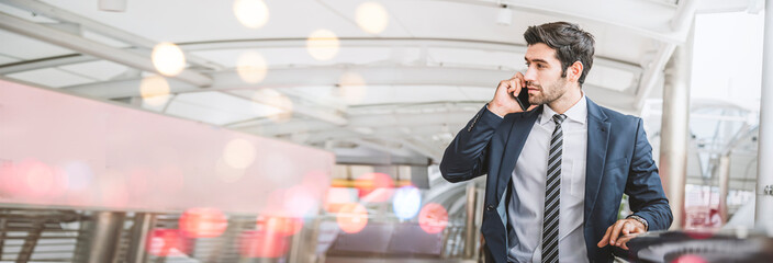Caucasian businessman in a suit using smartphone talking while standing outside the office, image...