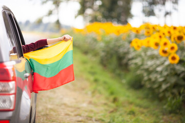Girl holding flag of Lithuania from the open car window driving on a beautiful road. Traveling in Lithuania, car tours, Independence day concept. Selective focus.