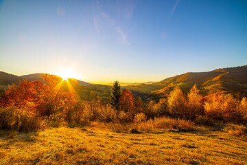 Sun sets behind forestry mountains in highland in autumn