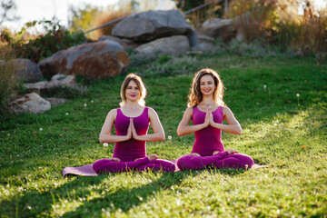 Two barefoot women practicing pilates or stretching with yoga block in park in a sunny summer day. Young and middle-aged caucasian women in pink sport clothing doing yoga exercises outdoors