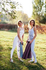 Photo of young ladies standing in bridge poses while training yoga together outdoors. Two women practicing yoga with beautiful view on background