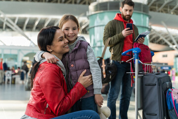 Smiling family with child at the airport. Happy mother embracing her little daughter while her husband standing at the background